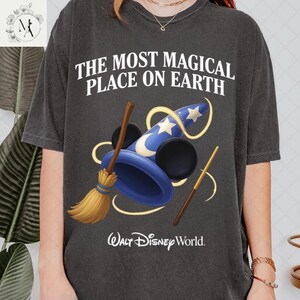A person wearing a black t-shirt with a graphic design featuring a wizard's hat, broom, and wand, along with the text "The most magical place on earth" and the Walt Disney World logo.