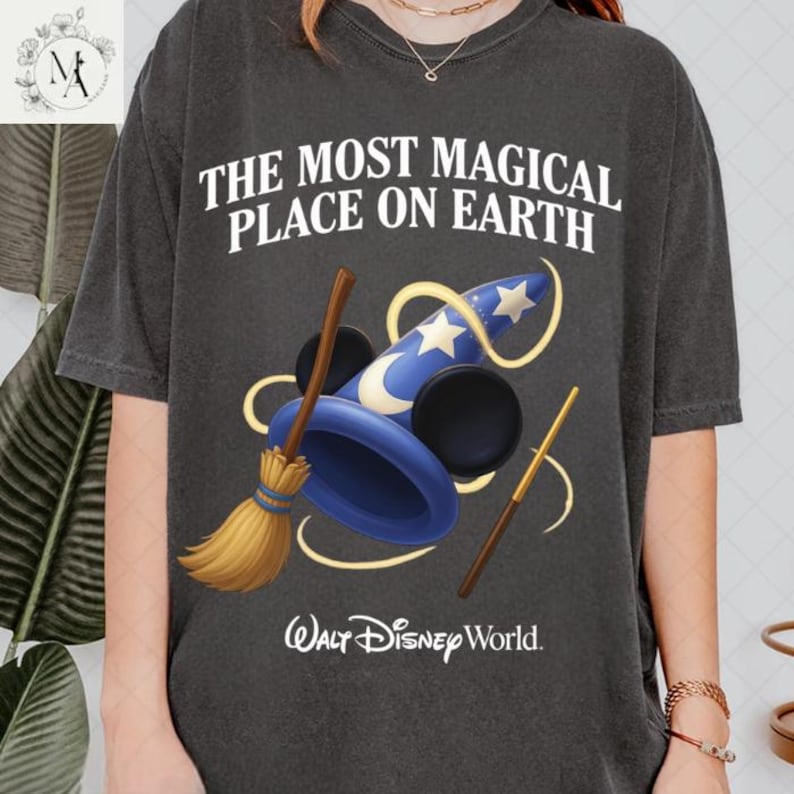 A person wearing a black t-shirt with a graphic design featuring a wizard's hat, broom, and wand, along with the text "The most magical place on earth" and the Walt Disney World logo.