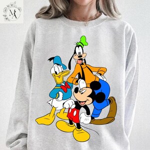 A person wearing a gray sweatshirt with a graphic of Disney characters, including Mickey Mouse, Donald Duck, and Goofy.