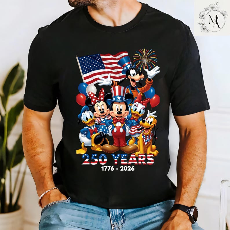 A black t-shirt with a graphic design featuring Disney characters Mickey Mouse, Minnie Mouse, Donald Duck, Goofy, and Pluto, along with an American flag and fireworks. The text below the image reads "250 YEARS 1776-2026".