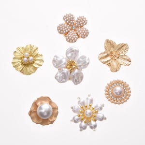 May include: An assortment of flower-shaped embellishments in gold and pearl. The designs include a gold flower with three pearls, a pearl-covered flower with a central gem, and a gold flower with a central pearl.