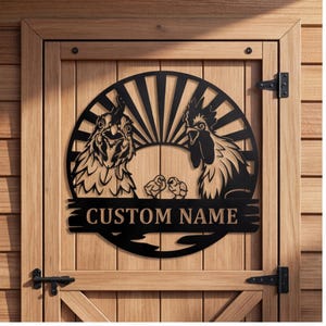 Könnte beinhalten: Ein rundes Wand-Schild aus schwarzem Metall mit einem Sonnenstrahlen-Motiv, einer Henne, einem Hahn und zwei Küken. Das Schild enthält einen horizontalen Balken in der Mitte mit dem Text CUSTOM NAME in fetter Schrift, montiert an einer Holztür.