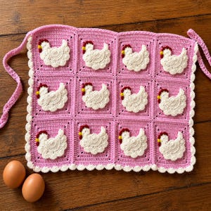 May include: A square crochet apron featuring a grid of twelve pink squares, each decorated with a white crocheted chicken motif. The chickens have red combs and yellow beaks. The apron is finished with a white scalloped border and pink ties.