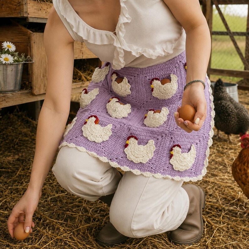 May include: A lavender crochet apron featuring a grid of square panels, each adorned with a white chicken appliqu&eacute; with a red comb. The apron has a scalloped white border along the bottom edge and is worn over white pants and a white ruffled top.