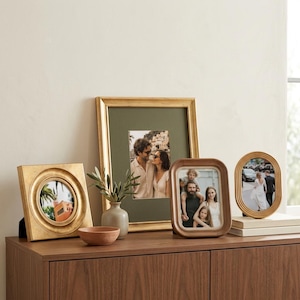 May include: A collection of four picture frames in various shapes and finishes, including a square gold frame with a circular opening, a large rectangular gold frame with a green mat, a rounded rectangular wood frame, and an oval wood frame.