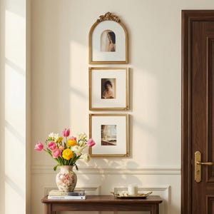 Puede incluir: Tres cuadros dorados con paspart&uacute;s blancos cuelgan de una pared color crema. El marco superior es arqueado. Un jarr&oacute;n con flores coloridas est&aacute; sobre una mesa de madera, junto con una bandeja y una vela. A la derecha hay una puerta marr&oacute;n oscuro.