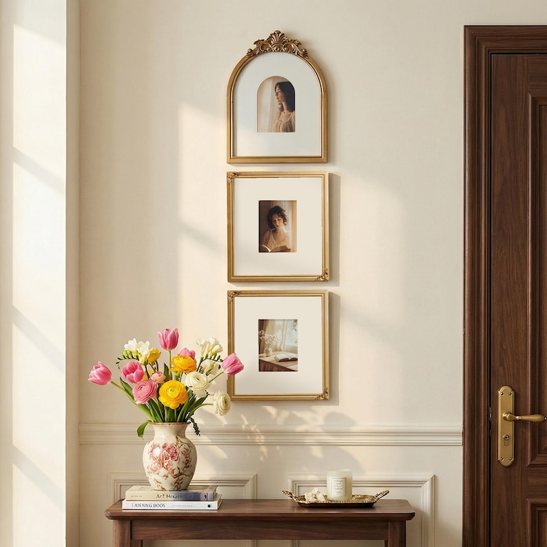 Puede incluir: Tres cuadros dorados con paspart&uacute;s blancos cuelgan de una pared color crema. El marco superior es arqueado. Un jarr&oacute;n con flores coloridas est&aacute; sobre una mesa de madera, junto con una bandeja y una vela. A la derecha hay una puerta marr&oacute;n oscuro.