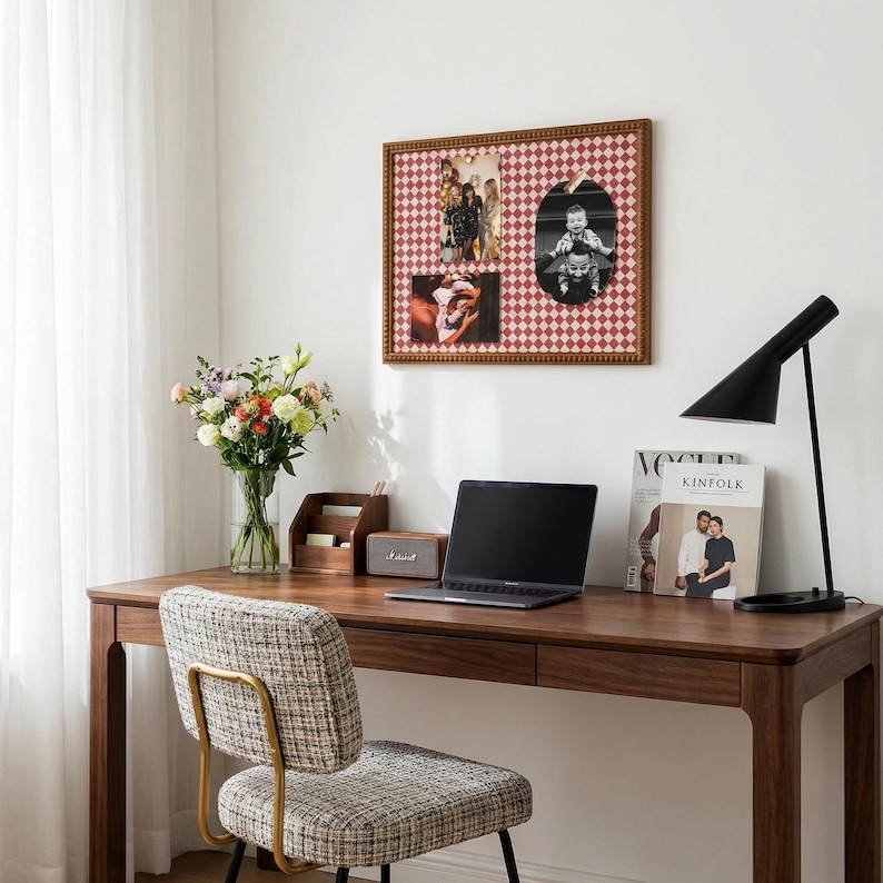 May include: A wooden desk with a laptop, lamp, and framed photos. A patterned chair sits in front of the desk. A vase of flowers and a magazine are also on the desk. The framed photos have a red and white diamond pattern.