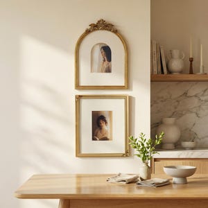 Puede incluir: Dos cuadros con marcos dorados cuelgan de una pared color crema. El marco superior es arqueado con detalles ornamentados, y el marco inferior es rectangular. Ambos marcos contienen retratos de mujeres. Una mesa de madera est&aacute; en primer plano.