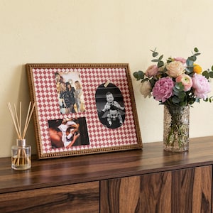 May include: A framed photo display with a red and white diamond pattern holds three photos. The frame is a warm brown color. A glass vase with a bouquet of pink, yellow, and white flowers sits to the right. A reed diffuser is on the left.