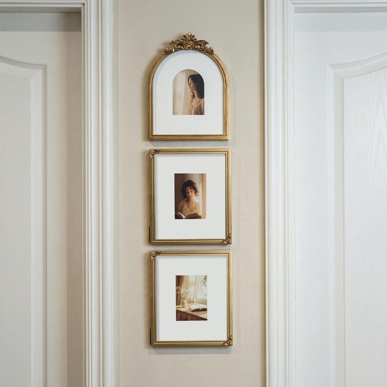 Puede incluir: Tres marcos dorados colgados en una pared beige. El marco superior es arqueado, los otros dos rectangulares. Cada marco contiene una fotograf&iacute;a con un paspart&uacute; blanco. Los marcos tienen detalles ornamentados.