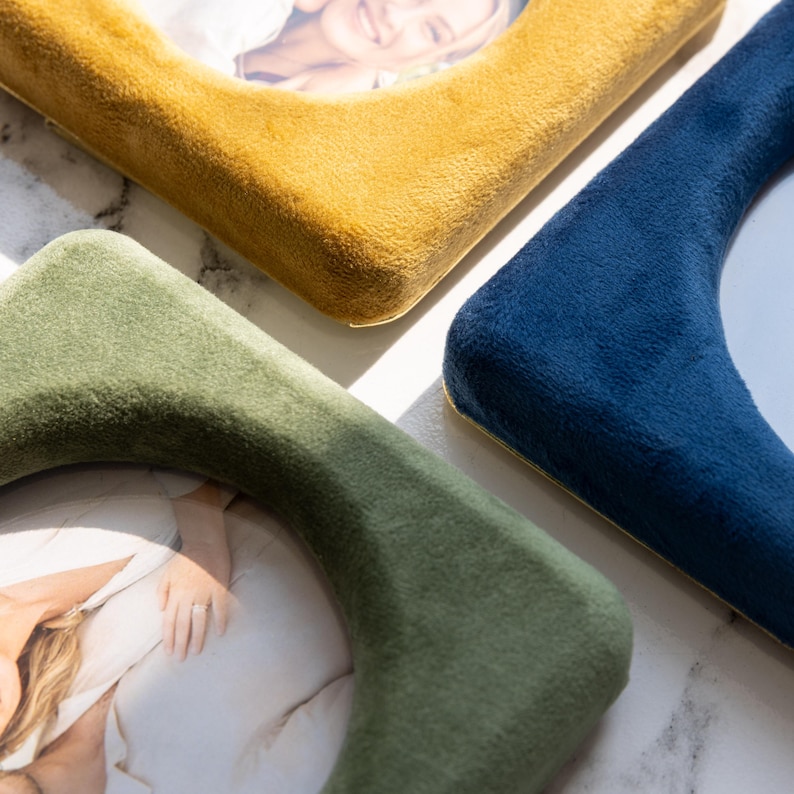 May include: Three square picture frames with rounded corners, each covered in a soft, plush velvet fabric. The frames are colored in mustard yellow, deep navy blue, and sage green, and each holds a photograph of a person.