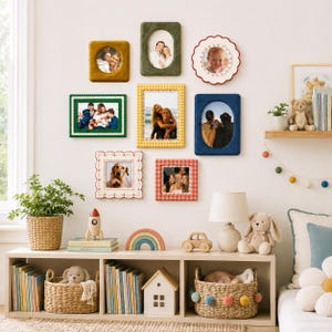 May include: A gallery wall featuring nine assorted picture frames in various shapes, colors, and textures, including velvet, scalloped, and patterned designs. The frames display family photographs and are arranged on a wall above a wooden shelf.