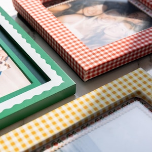 May include: Three rectangular picture frames featuring distinct patterns. One frame has a red and white gingham check, another is solid green with a white scalloped inner border, and the third has a yellow and white gingham check pattern.