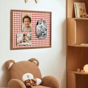 May include: A wooden framed memo board with a red and white diamond pattern. The board holds three photos, two rectangular and one oval, secured with a wooden clip. The frame has a beaded border. A large teddy bear chair is in the foreground.