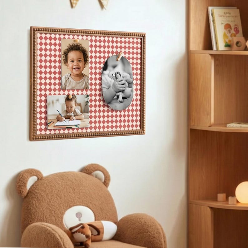 May include: A wooden framed memo board with a red and white diamond pattern. The board holds three photos, two rectangular and one oval, secured with a wooden clip. The frame has a beaded border. A large teddy bear chair is in the foreground.