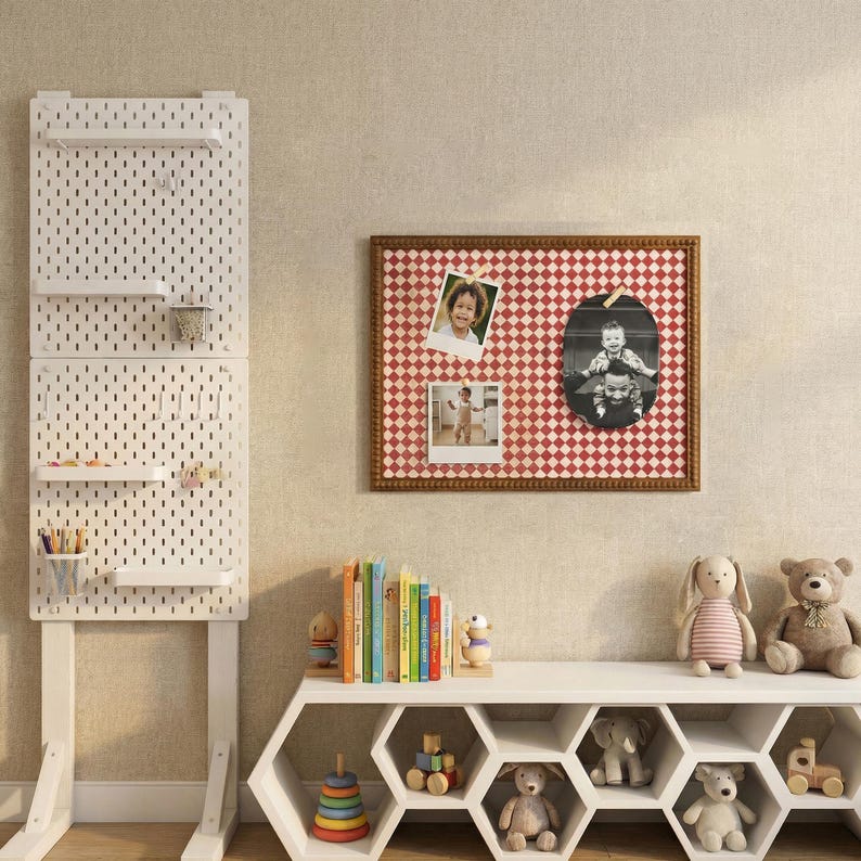 May include: A white pegboard with shelves and accessories stands next to a red and white checkered bulletin board with photos. A white hexagonal shelf holds books, toys, and stuffed animals, creating a cozy, organized space.