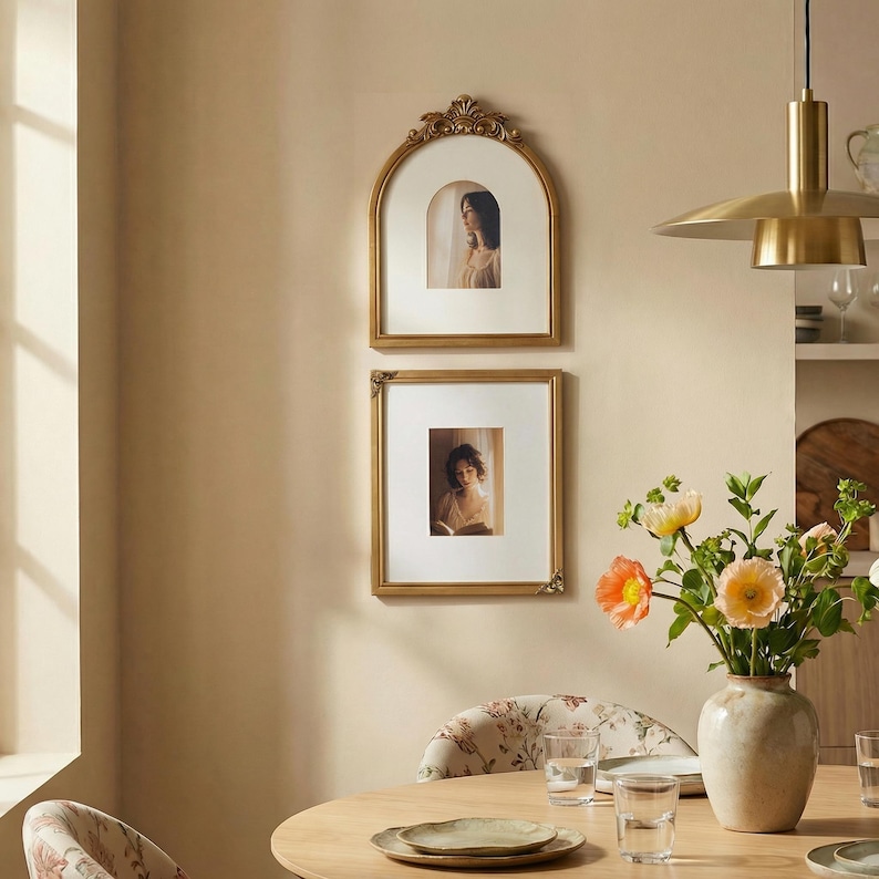 Puede incluir: Dos marcos dorados cuelgan de una pared beige. El marco superior es arqueado con detalles ornamentados, mientras que el inferior es cuadrado. Cada marco contiene una fotograf&iacute;a en blanco y negro de una persona.
