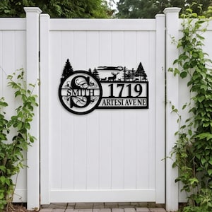 May include: A black metal sign featuring a circular monogram with the letter S and the name SMITH. To the right, the number 1719 is displayed above the text ARTESI AVE NE. The top section depicts a forest scene with pine trees and a deer.