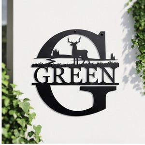 May include: Black metal wall art featuring a deer silhouette within a stylized landscape. The word "GREEN" is displayed prominently within a large letter "G". Decorative outdoor sign for home decor.