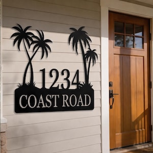 May include: Black metal address sign with palm tree silhouettes, the number 1234, and the words COAST ROAD in white. The sign is mounted on a light beige wall next to a wooden door.