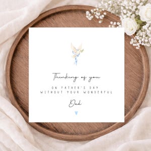 May include: A white card with the text "Thinking of you on Father's Day without your wonderful Dad" is displayed on a wooden tray. The card features a dove illustration with blue accents and a small blue heart.