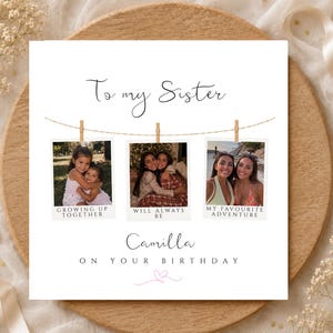 May include: A square greeting card with the text To my Sister and Camilla on your birthday. It features three hanging photo prints on a string with clothespins, labelled Growing up together, Will always be, and My favourite adventure, plus a pink heart.