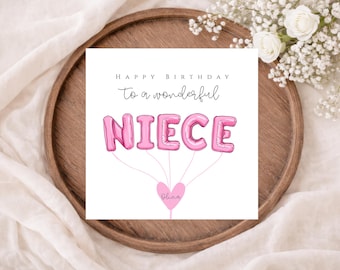 May include: A birthday card with the words "HAPPY BIRTHDAY to a wonderful NIECE" in black and pink. The word "NIECE" is written in pink balloon letters. The card is on a wooden tray with white flowers.