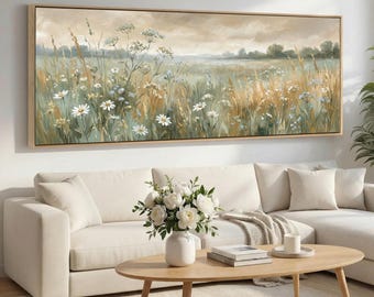 Könnte beinhalten: Ein rechteckiges, gerahmtes Leinwandkunstwerk, das ein Feld mit Wildblumen und hohem Gras in Grün-, Beige- und Weißtönen zeigt. Das Kunstwerk hängt über einem weißen Ecksofa und einem Holztisch mit einer Vase mit weißen Blumen.