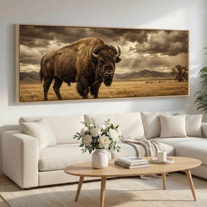 May include: A rectangular wall art print featuring a large brown bison standing in a vast golden prairie. The background displays rolling mountains under a dramatic, cloudy sky with light rays breaking through the dark, heavy clouds above.