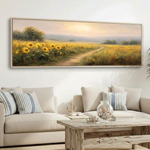 May include: A rectangular framed painting shows a sunflower field under a bright sky. A dirt path weaves through the yellow flowers, leading to the horizon. The artwork is displayed above a beige sofa with striped cushions.