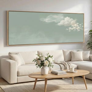 May include: A large rectangular framed artwork shows a tranquil sky with soft, white clouds against a muted green backdrop. Below, a white sofa, a wooden coffee table, and a vase of white flowers enhance the room's calm aesthetic.