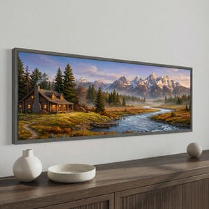 May include: A panoramic framed wall art print depicting a rustic log cabin with a stone chimney beside a winding river. The scene features a dense evergreen forest, a small wooden canoe at the water's edge, and snow-capped mountain peaks.
