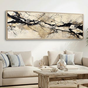 May include: Abstract artwork in a rectangular, light-coloured wooden frame. The piece features a beige background with black and brown linear patterns. It is displayed above a beige sofa with striped cushions.