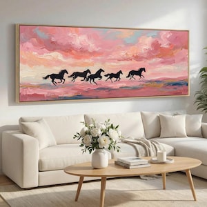 Könnte beinhalten: Ein gerahmtes Leinwandkunstwerk zeigt fünf schwarze Pferde, die vor einem rosa-pfirsichfarbenen Himmel mit Wolken laufen. Das Kunstwerk hängt über einem weißen Sofa in einem Wohnzimmer.