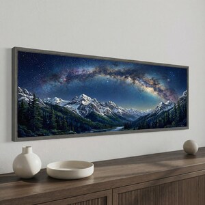 May include: Panoramic framed artwork depicting a mountain range under a starry night sky. The artwork features snow-capped peaks, dark green forests, and a river. The night sky is filled with the Milky Way galaxy, with shades of blue, purple, and yellow.