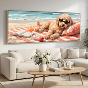 May include: A horizontal wall art print featuring a golden doodle dog wearing black sunglasses, lying on a red and white striped beach towel on the sand. Beside the dog is an open book, a glass of orange liquid, a glass of water, and a red apple.