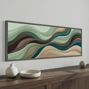 May include: Abstract art print in a rectangular, dark gray frame. The artwork features flowing, layered waves in shades of green, brown, and teal. The print is displayed above a wooden cabinet, with a white vase, a white bowl, and a small white sphere.