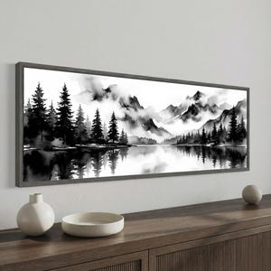 May include: A framed panoramic watercolor painting of a mountain landscape in shades of gray and black. The artwork depicts a serene scene with a lake reflecting the trees and mountains. The frame is a dark gray color.