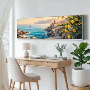 May include: A framed landscape painting depicts a coastal scene with a town, sea, and mountains. The artwork features a vibrant color palette with blues, yellows, and greens. A lemon tree with ripe yellow fruit is in the foreground. The painting is displayed above a wooden desk.