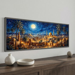 May include: A framed panoramic painting depicts a Middle Eastern city at night. The artwork features golden-domed buildings, palm trees, and a full moon in a starry sky. The painting is set in a gray frame and is displayed on a wooden surface.