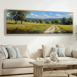 May include: A landscape painting in a light wood frame depicts a sunny field with a dirt road. Yellow wildflowers and green trees dot the scene under a blue sky with fluffy white clouds. The artwork hangs above a beige sofa with striped pillows.