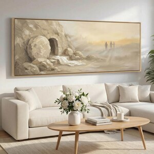 May include: A framed landscape painting depicts a sepia-toned scene of a tomb with a large stone and figures in the distance. The artwork is displayed above a white sectional sofa, with a wooden coffee table and a vase of white flowers.