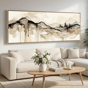 Puede incluir: Impresión artística de paisaje abstracto en un marco de madera rectangular. La obra presenta un diseño de acuarela con siluetas de montañas negras y marrones, salpicaduras y goteos sobre un fondo crema. La pieza se exhibe sobre un sofá blanco.
