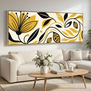 May include: A rectangular canvas art print with a floral design in yellow and black on an off-white background. The artwork is framed in a light wood colour and hangs above a white sofa and coffee table.