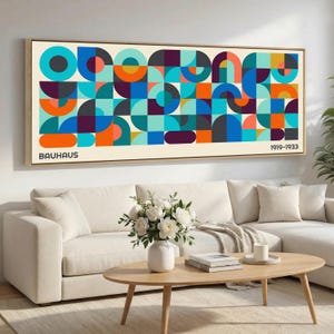 May include: A framed Bauhaus art print featuring a geometric design in shades of blue, orange, teal, and purple. The print includes the text "BAUHAUS" and "1919-1933". The artwork is displayed above a white sofa and wooden coffee table.
