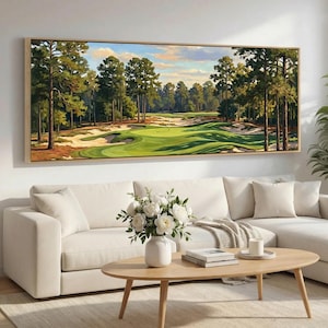 May include: A rectangular framed painting depicting a golf course scene with green fairways, sand traps, and tall trees. The artwork hangs above a white sofa and a wooden coffee table, creating a calm living room setting.