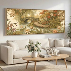 May include: A framed art print of a garden scene with a stone bridge, wooden walkway, and pond with water lilies. The artwork uses a palette of greens, browns, and oranges. Two hummingbirds are visible. The frame is a light wood colour. The print is a decorative item.