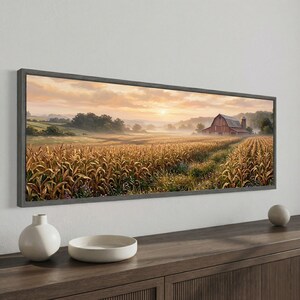 Peut inclure: Une impression d'art panoramique encadrée représentant un paysage rural avec un champ de maïs doré au premier plan, une grange rouge avec un silo au loin, et un ciel de lever de soleil doux avec des nuages brumeux sur des collines dans un cadre gris foncé.
