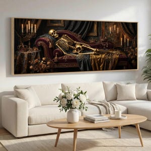 May include: A framed artwork depicts a golden skeleton reclining on a burgundy chaise lounge. The scene is illuminated by candlelight, with dark drapes and ornate details. The artwork is displayed above a white sofa in a living room setting.
